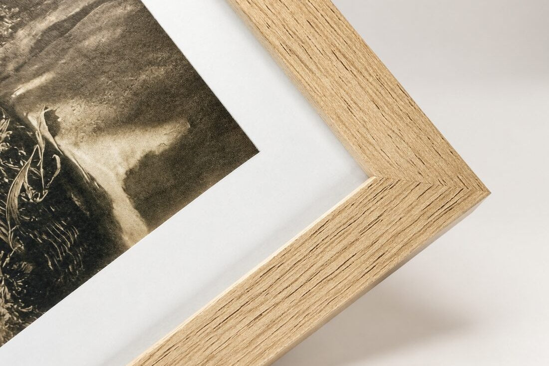The corner of a light oak frame around a print with a white border.