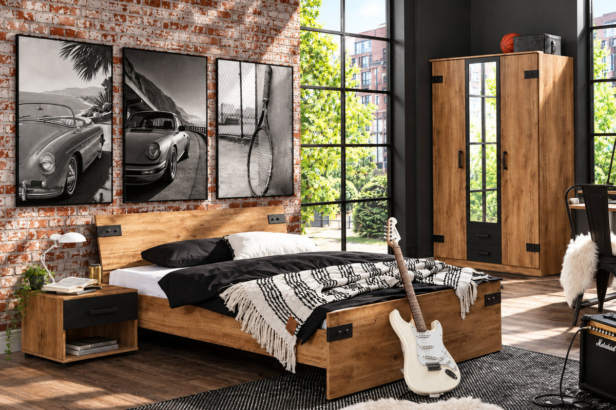 Chambre avec mur de brique, lit sombre, guitare et trois affiches en noir et blanc dans des cadres noirs.