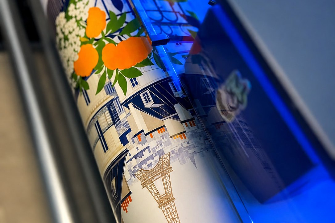 Une affiche sort du traceur dans l'atelier de Grasse, motif d'oranges et de toits parisiens sur le rouleau.