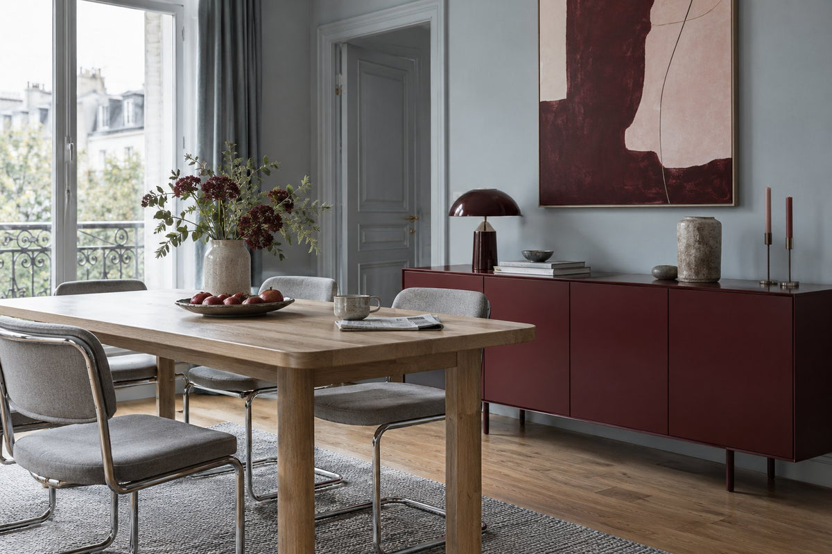 Burgundy sideboard against blue-grey walls with pale wood and grey metal chairs