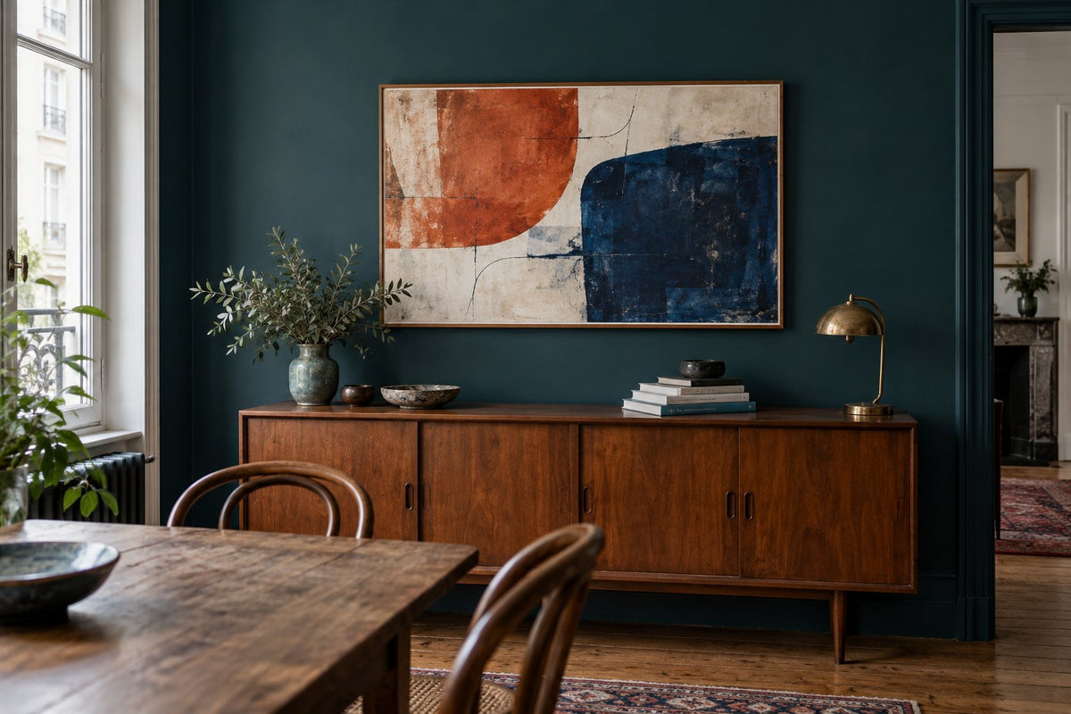Credenza in noce davanti a una parete verde-blu, con una grande composizione astratta arancione e blu e oggetti quotidiani.