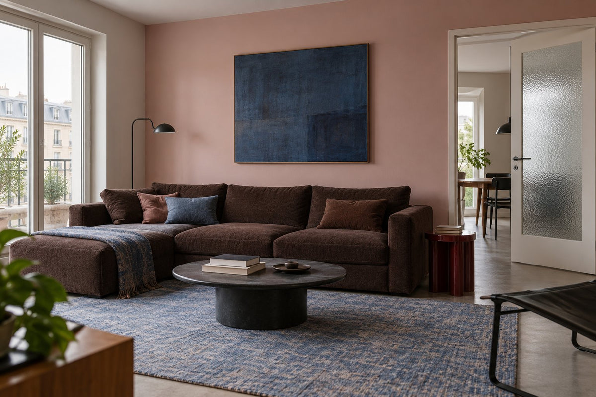 Chocoladebruine bank, vergrijsd roze muur en blauw schilderij in een lichte woonkamer