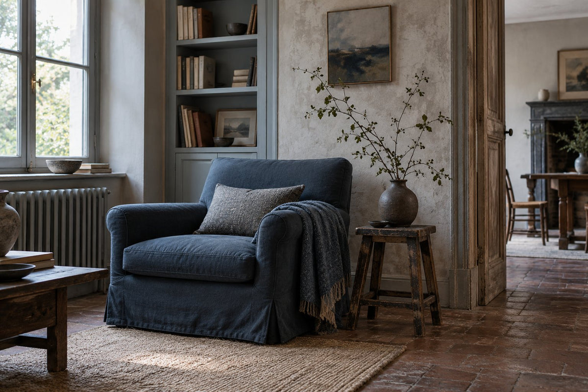 Sobere leeshoek met leiblauwe fauteuil, gepatineerd hout en luchtige botanische compositie