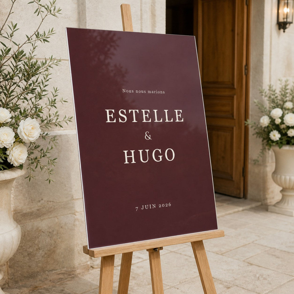 Panneau de bienvenue de mariage en plexiglass bordeaux, posé sur un chevalet à l'entrée du lieu de réception