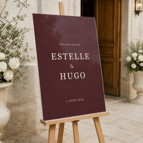 Panneau de bienvenue de mariage en plexiglass bordeaux, posé sur un chevalet à l'entrée du lieu de réception