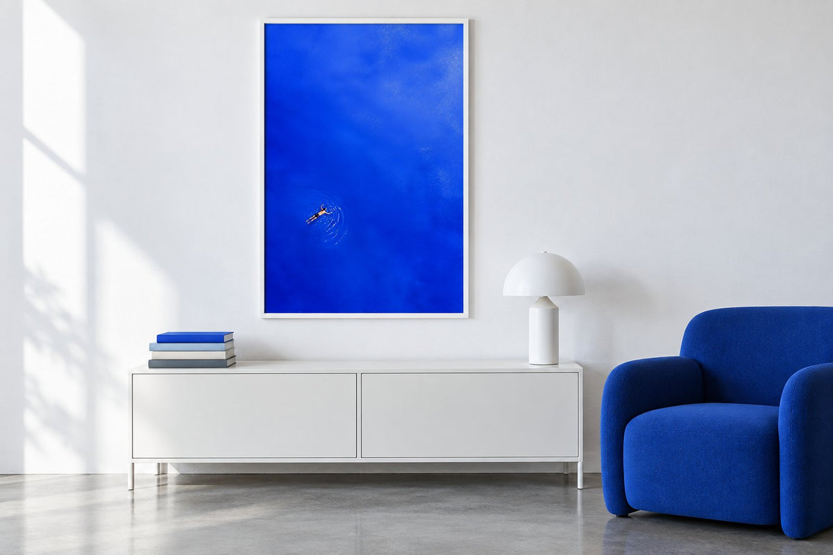 Simulation eines weißen Wohnzimmers mit blauem Sessel, Schwimmerposter, Lampe und Bücherstapel auf dem Möbel