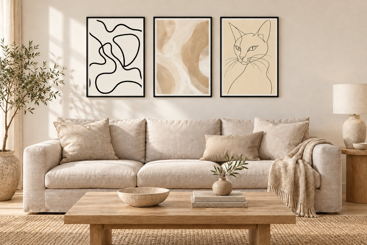 Dieselben drei Poster in schwarzen Rahmen an derselben cremefarbenen Wand über dem hellen Sofa.