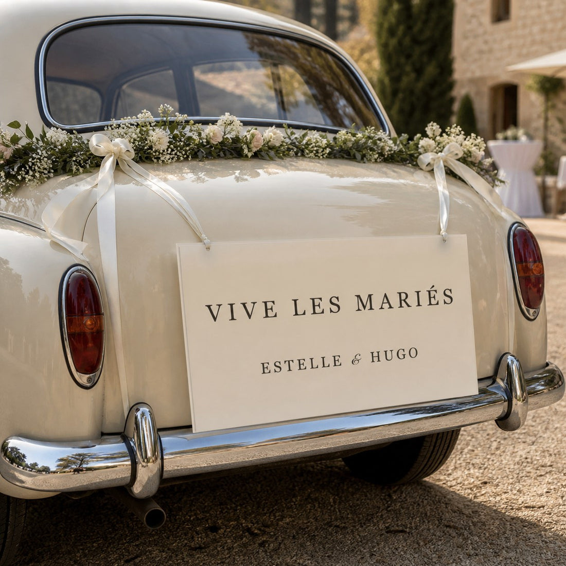 Cartello di matrimonio crema appeso sul retro di un’auto d’epoca decorata con fiori.