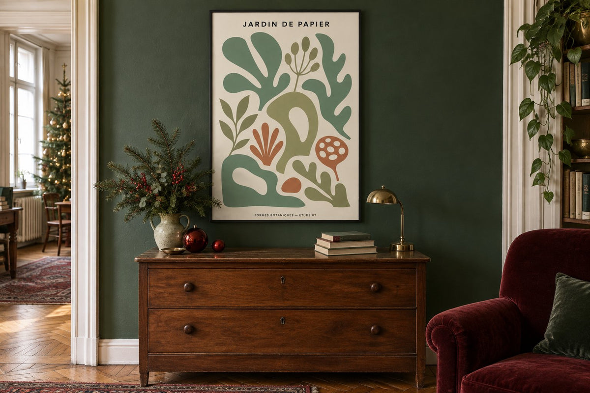 Simulation de Noël avec une affiche botanique en cadre noir, un mur vert, une commode en noyer, un fauteuil bordeaux et un sapin à gauche